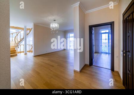 A large open living room with a staircase leading up to the second floor. The room is empty and features a chandelier hanging from the ceiling Stock Photo