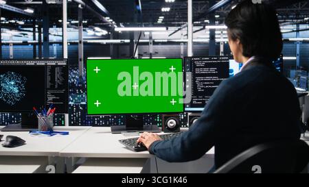 Data center admin typing on isolated screen PC keyboard, using AI. IT specialist at work using artificial intelligence on chroma key computer to oversee servers powering deep learning, camera A Stock Photo