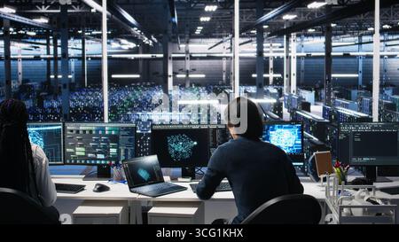 Data center technician entering office, managing AI systems for uptime and efficiency. IT professional arriving at work, sitting at desk, using artificial intelligence in server hub, camera A Stock Photo