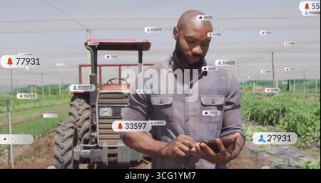 Holding tablet, man monitoring notification icons under shade net with red tractor in field Stock Photo