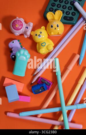 Colorful pencils, pens, erasers, sharpeners, and fun pencil sharpeners are arranged on a vibrant orange surface, ready for the back-to-school season Stock Photo