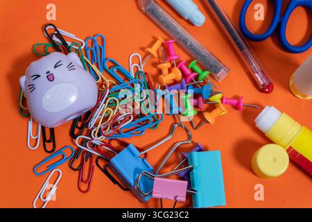 Colorful stationery items creating a vibrant and disorganized arrangement on an orange backdrop Stock Photo