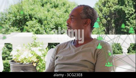 Sitting man in grey t-shirt gazing left on home patio, flowering planter, green digital icons Stock Photo