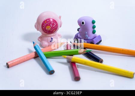 School supplies including colored pencils, a dinosaur eraser and an astronaut pencil sharpener rest on a white surface, ready for creative endeavors Stock Photo