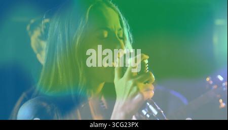 Singing vocalist holding vintage microphone on music stage, with colored lights and electric guitar Stock Photo