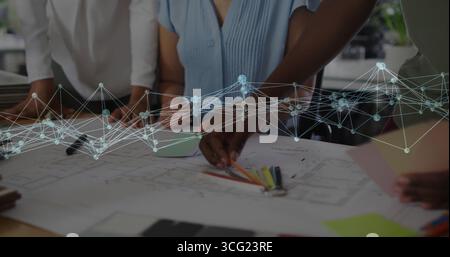 Project team in business attire pointing at blueprints on office table, with digital overlay Stock Photo