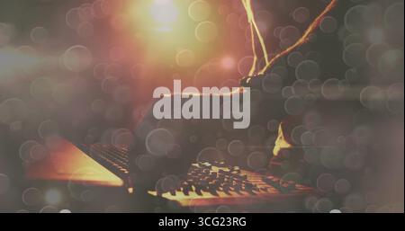Twisting DJ arm in dark sleeve adjusting mixer knobs on nightclub stage, with warm light bokeh Stock Photo