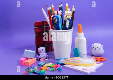 Various colorful school supplies arranged on a vibrant purple background, creating a cheerful back-to-school atmosphere Stock Photo