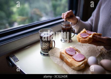 Train lunch sandwiches and tea in metal cup holders. Passenger have lunch by window in travel Stock Photo