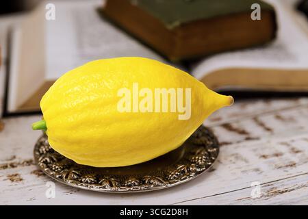 Jewish festival of Sukkot traditional symbols yellow etrog is placed on silver dish next to an open book Stock Photo