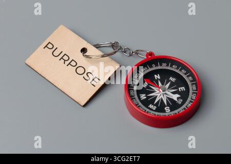 A close-up image of a small, red compass and a wooden keychain tag with the word "PURPOSE". Finding one's purpose or having a clear direction in life Stock Photo