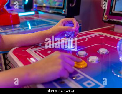 A person's hands gripping a joystick and pressing buttons on an arcade game machine. Nostalgia, fun, and entertainment from classic arcade gaming Stock Photo