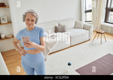 Caucasian Senior Woman Wearing Headphones Using Smartphone While Exercising Stock Photo