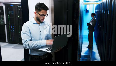 Data center, cybersecurity and man with laptop, coding and network engineer with tech for software. Server room, IT specialist and person with Stock Photo