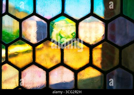 Vibrant hexagonal stained glass creates a colorful mosaic effect, blending shades of yellow, blue, green and pink. Light passing through textured Stock Photo