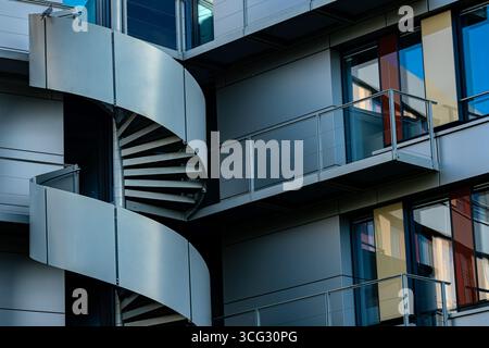 A contemporary building features an elegant spiral staircase, complemented by glass balconies and sleek facade panels. The structure showcases modern architectural design elements. Stock Photo