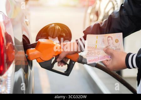 Hand of a man refueling the car and holding two thousand one hundred baht banknote, concept of rising fuel prices. Stock Photo