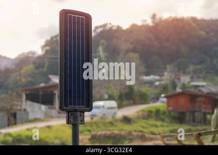 Lighting pole with photovoltaic panel and LED lamp lights with green rural village background. Close-up, selective focus. Stock Photo