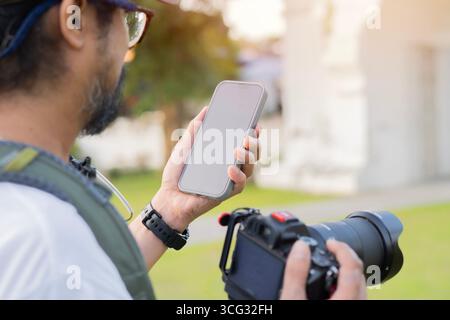 Shot of Asian male traveler or photographer using a mobile phone on sidewalk of buddhist temple in Thailand Stock Photo