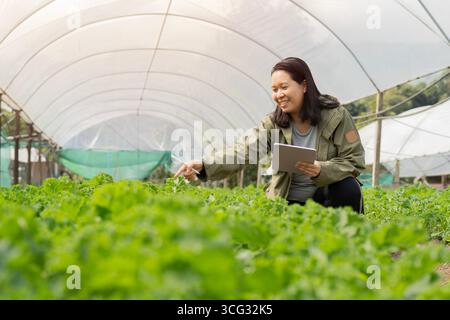 Farmer using laptop computer to conduct research in a greenhouse. Side view, selective focus. Stock Photo