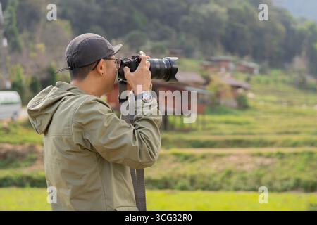 Young cheerful man photographer taking photographs with digital camera in a mountains, Travel and active lifestyle concept. Stock Photo