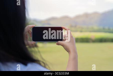 Back view of woman holding phone over scenery background. Accessibility of mobile communications and the Internet Stock Photo