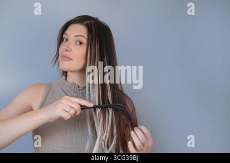 Young woman gently combing hair extensions with wide tooth comb comfortable hair care in beauty salon Stock Photo