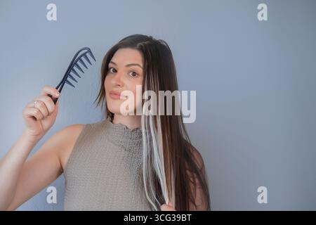 Beautiful long hair extensions young woman using special comb for gentle hair care in professional beauty salon Stock Photo