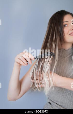 Young woman caring for long hair extensions using comfortable comb for gentle and smooth hair styling Stock Photo