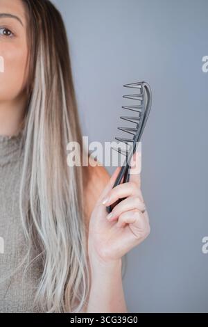 Woman combing hair extensions comfortably using wide tooth comb to prevent tangles and hair breakage Stock Photo