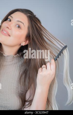 Special comb for hair extensions young woman gently caring for strands in professional beauty salon Stock Photo