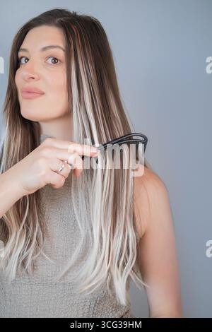 Young woman gently combing hair extensions with comfortable wide tooth comb for safe and easy styling Stock Photo