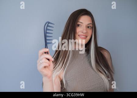 Beautiful hair extensions woman using comb for gentle and comfortable hair care in professional beauty salon Stock Photo