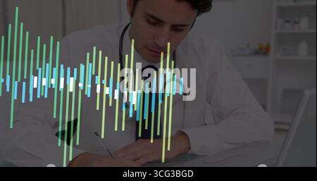 Physician wearing lab coat writing notes on pad at medical office desk, with stethoscope and laptop Stock Photo