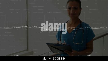 Doctor wearing scrubs and stethoscope holding tablet and stylus in clinic corridor, copy space Stock Photo