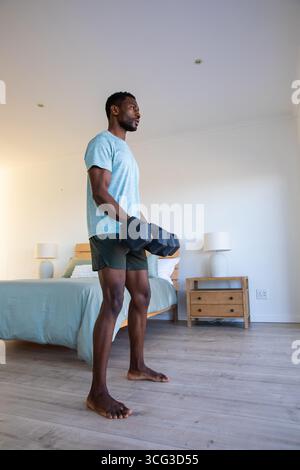 African american man lifting hexagonal dumbbells in tidy bedroom beside wooden bed, lamps Stock Photo