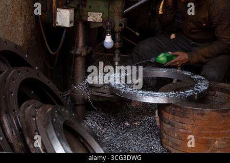 This image shows a close-up of metal machining, with a worker using lubricant on a circular flange surrounded by metal shavings and tools, Stock Photo