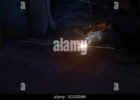 This image depicts a close-up of a welding torch in use, with bright sparks and smoke illuminating a dark workspace, Stock Photo