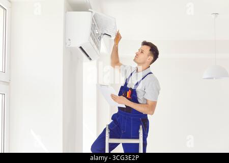 AC maintenance and repair service worker with clipboard checks air conditioner on wall Stock Photo
