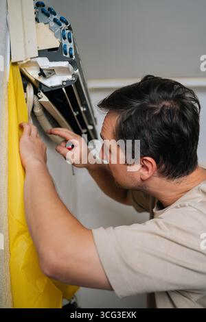 Close-up of skilled HVAC professional disassembling wall-mounted air conditioning unit, using yellow drainage bag while carefully accessing electrical Stock Photo