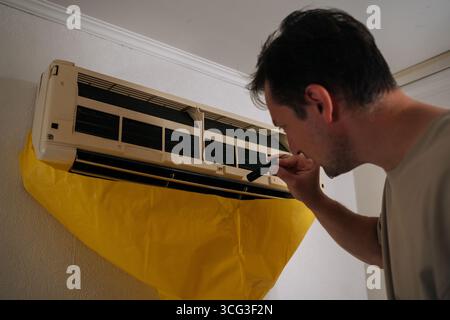 Close-up of HVAC technician using flashlight, inspecting air conditioning unit covered with yellow drop cloth during maintenance or repair service. Stock Photo