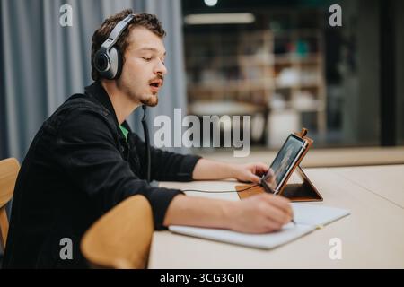 Young man studying with headphones using a tablet at a desk Stock Photo
