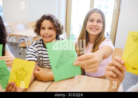 A group of children in a classroom environment holding cards with food images, engaging in an interactive learning activity about healthy food choices Stock Photo