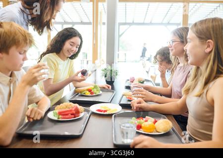 A group of schoolchildren having lunch in a clean cafeteria, enjoying nutritious meals together in a positive and friendly environment. The table is s Stock Photo