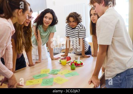 A group of children in a classroom setting engaged in a discussion about nutrition, focusing on fresh fruits and vegetables. Promotes learning, teamwo Stock Photo
