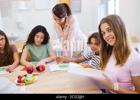 A group of students and a teacher learning together in a classroom setting, featuring fresh fruits and vegetables on the table, representing healthy e Stock Photo