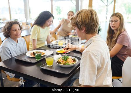 A gathering of students sharing a lunch in a school cafeteria, fostering social interactions and friendships among peers while enjoying healthy meals Stock Photo