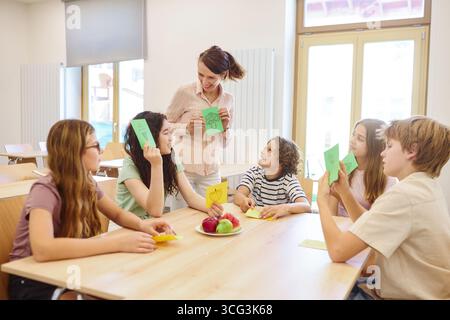 Happy students and a teacher interacting in a school cafeteria, discussing healthy foods. Apples and fruits enhance the educational experience in a ch Stock Photo