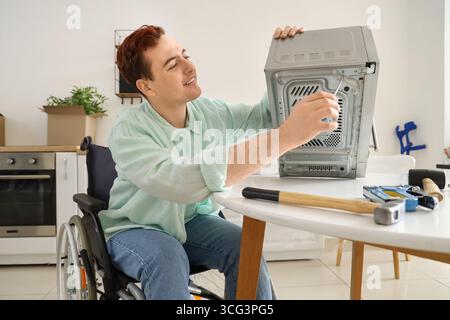 Young man in wheelchair repairing microwave oven at home Stock Photo