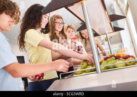 A group of students choosing fruits from a fresh produce display in the school cafeteria. They interact positively while selecting nutritious options, Stock Photo